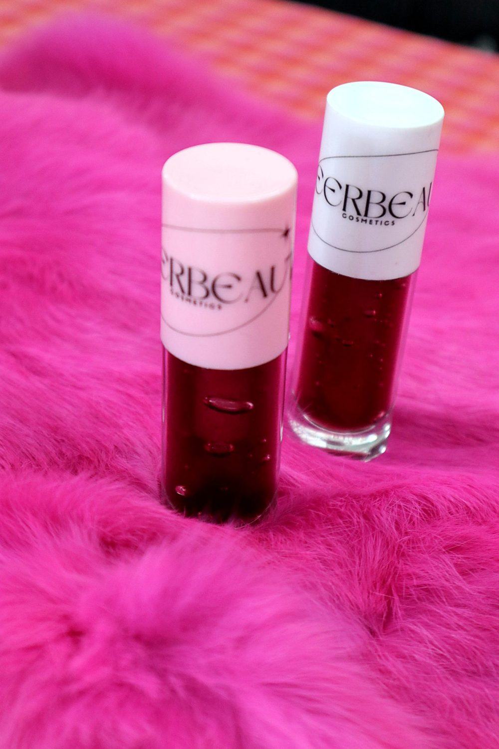 Two MEERBEAUT glosses with pink and white caps on pink fur, from our market table