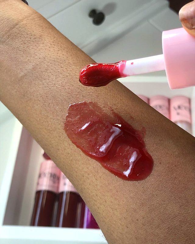 A swatch of red lip gloss on an arm, with the wand beside it