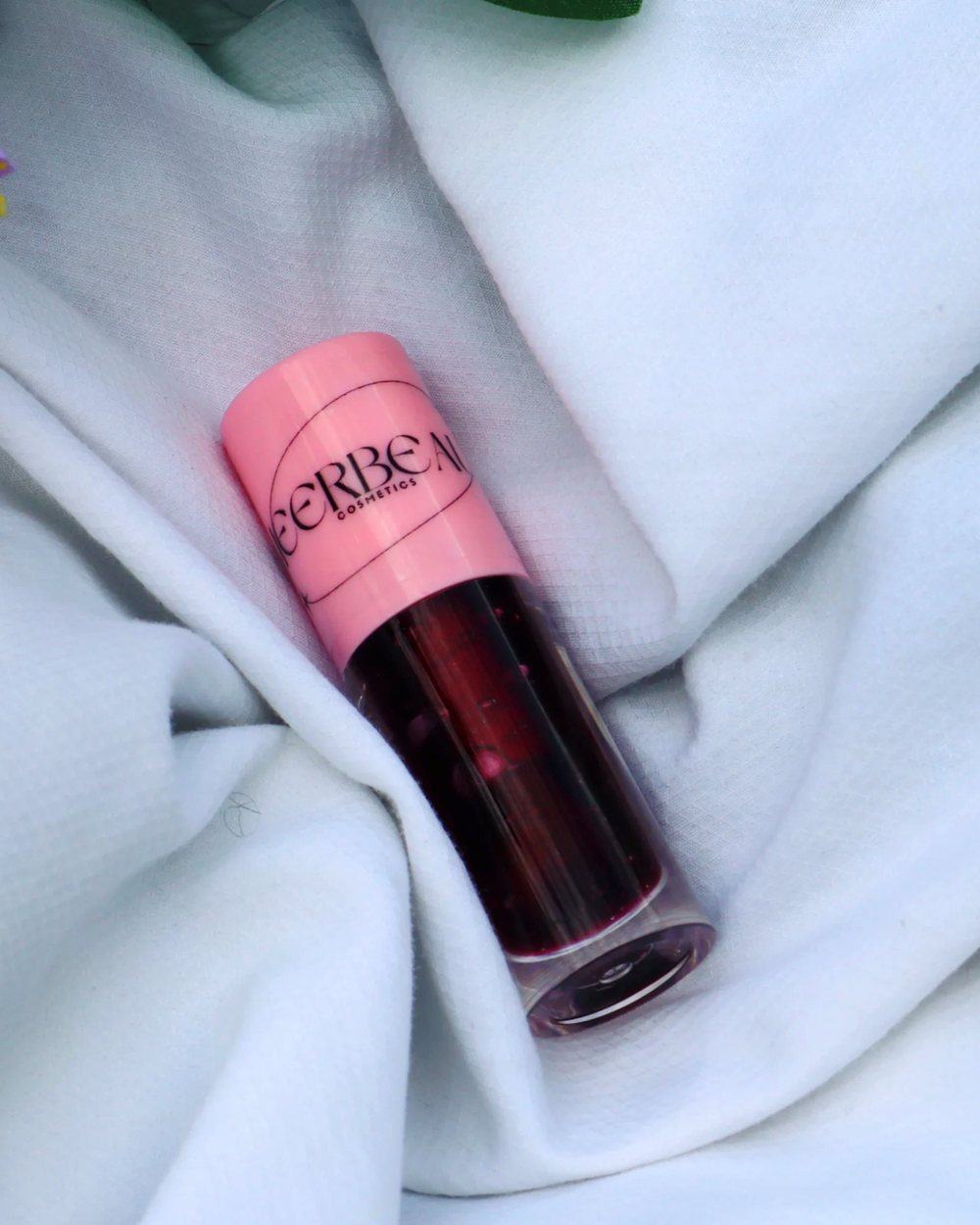 Lust, a deep tinting gloss in a pink-capped MEERBEAUT wand tube on white fabric
